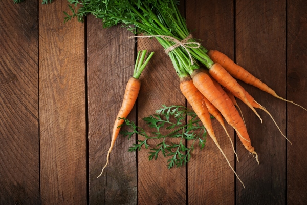 bunch of fresh carrots with green leaves over wooden table - Овощи, бобовые, грибы: полезные советы