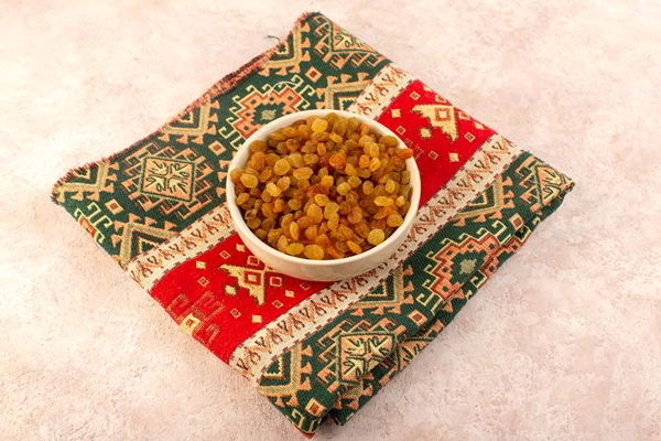 a top view orange dried raisins inside round plate on colorful designed carpet on pink - Паренки из моркови с изюмом