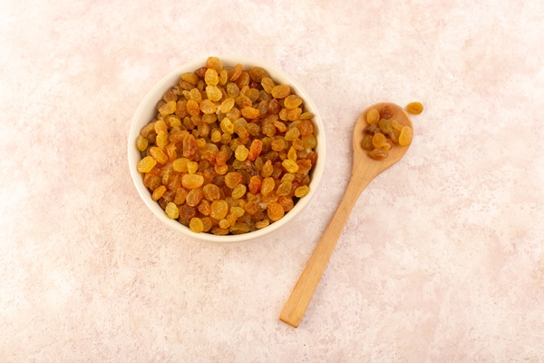 a top view orange dried raisins inside white round plate with wooden spoon on pink - Постные блинчики со сладкой морковью и изюмом