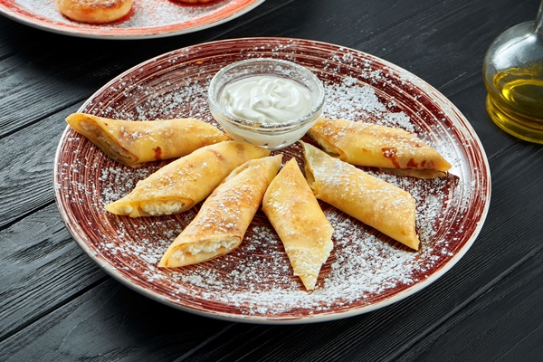 close up view on tasty french crepes stuffed with cottage cheese and sour cream in a ceramic plate on dark wooden surface - Постные блинчики с рисом и изюмом