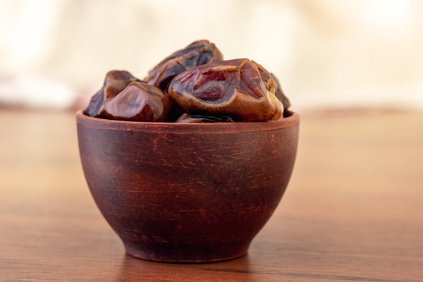 dry tasty dates in a brown ceramic cup on a blurred background - Постные блинчики с сиропом из сухофруктов