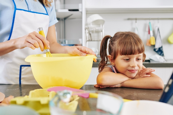 smiling little girl leaning on kitchen counter and watching cartoon on tablet computer when her mother making pancake dough in the morning - Постные гречневые блины на закваске