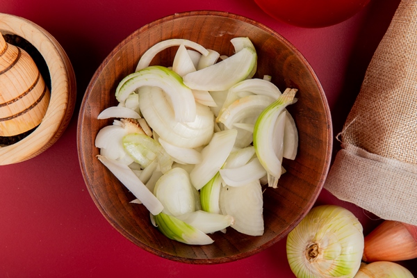 top view of sliced white onion in bowl with whole ones spilling out of sack and black pepper in garlic crusher on red - Грибная аджика