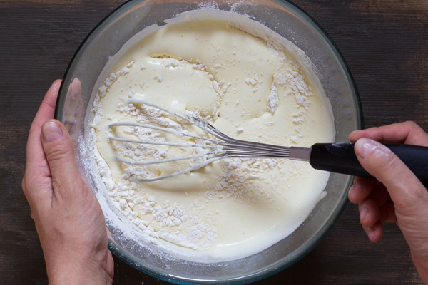 top view of woman hand mixing with whisk dry ingredients and batter on wooden background - Постные блинчики с начинкой из шпината