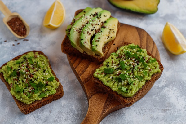 avocado open toast with avocado slices lemon flax seeds sesame seeds black bread slices top view - Бутерброд с авокадо и чесноком