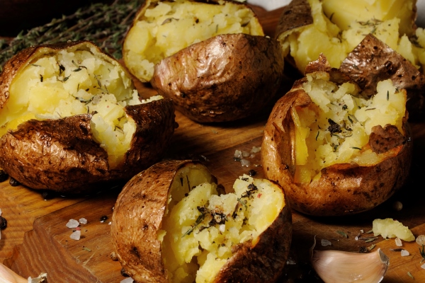 broken baked potato with spices and herbs on a wooden board - Картофель печёный