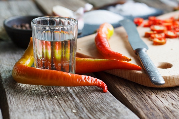 close up of a vinegar glass and whole pepper next to a board with chopped chili peppers on an old wooden surface - Соус "Сацебели"