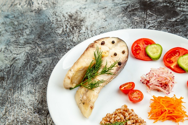 close up shot of boiled fish buckwheat served with vegetables green on a white plate on ice surface with free space - Судак разварной под разными соусами