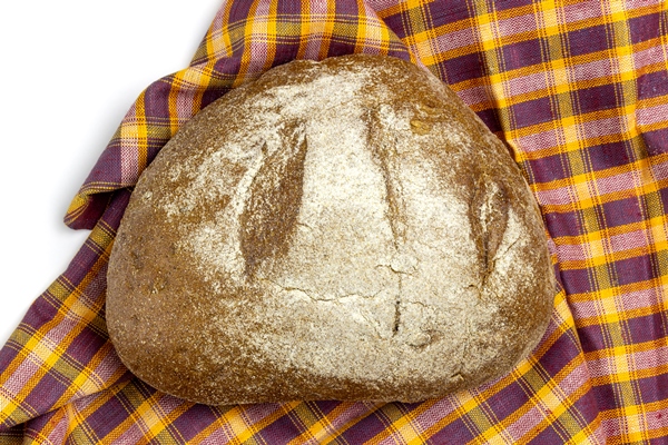 fresh loaf of whole grain black bread lies on a burgundy yellow and orange kitchen towel - Русский квас