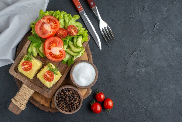 front close view of chopped and whole fresh vegetables cheese on cutting board and spices on the right side on black surface - Перекус "Отличник"