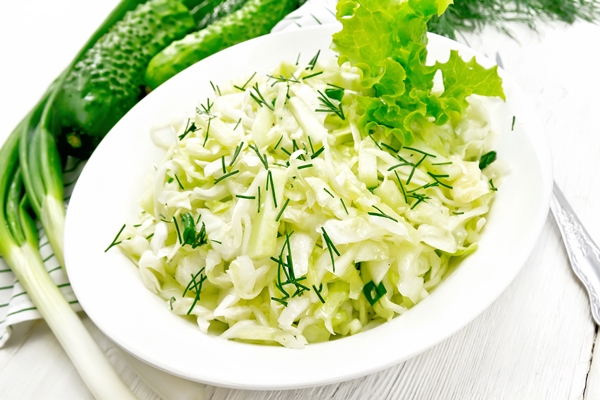 Свежая шинкованная капуста salad of fresh cabbage green onions and cucumber with vinegar and vegetable oil dressing in a plate towel dill and fork on light wooden board background - Свежая шинкованная капуста