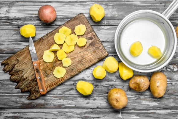 sliced potatoes on a cutting board with a knife and peeled potatoes in a saucepan on wooden surface - Постный суп грибной с галушками