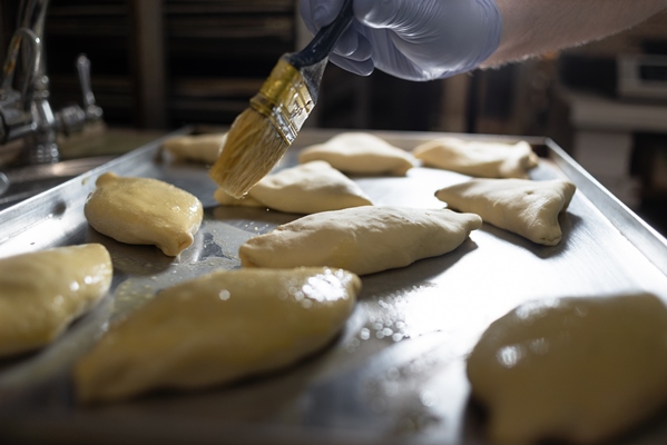 the cook greases small pies on a metal baking sheet with a brush and vegetable oil raw dough in the kitchen at the bakery flour products and products - Постное тесто на дрожжах для пирожков и пирогов