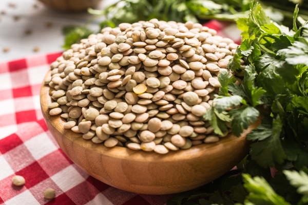 uncooked lentils in wooden bowles with parsley herbs on kitchen table - Чечевица с грибами, постный стол