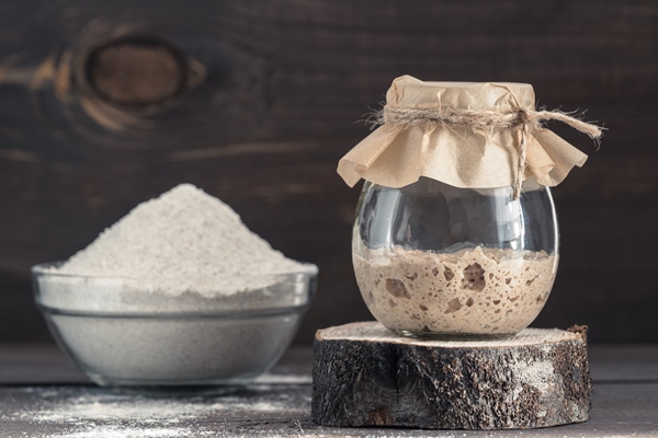 active rye sourdough starter in glass jar and rye flour on brown wooden background starter for sourdough bread toned image copy space 1 - Солдатский квас-сыровец из хлеба (рецепт XVIII века)