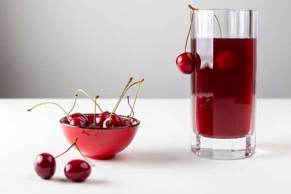 Вишнёвый квас front view of cherry juice inside long glass with fresh cherries on the white surface - Вишнёвый квас