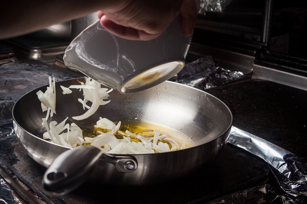 side view frying onions with pan and deep plate and human hand in stove - Щи валаамские с сухими грибами