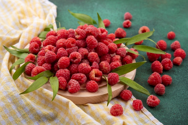 side view of raspberries with leaves on cutting board on plaid cloth and on green 1 - Малиновый квас