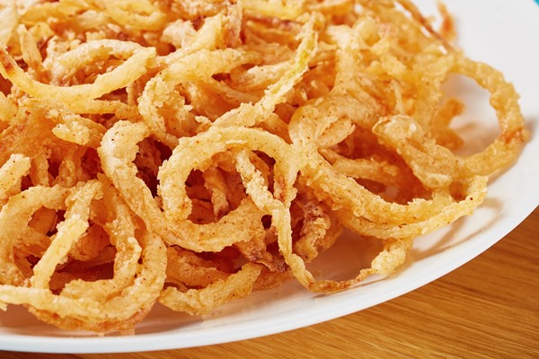 close up of crispy fried onions with fresh spinach and tomato salad on a white plate on a wooden board view from above - Блинчики с рыбой и маринованными огурцами