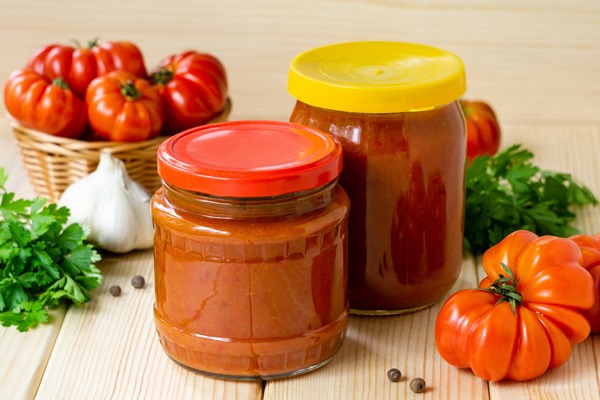 homemade tomato hot sauce with garlic and pepper in glass jars on wooden table - Постная аджика острая