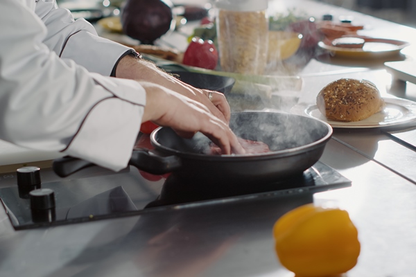 male chef putting meat steak to cook in frying pan with olive oil making delicious meal dish person cooking beef on stove to prepare cuisine food with culinary recipe close up hnadheld shot - Жареное мясо