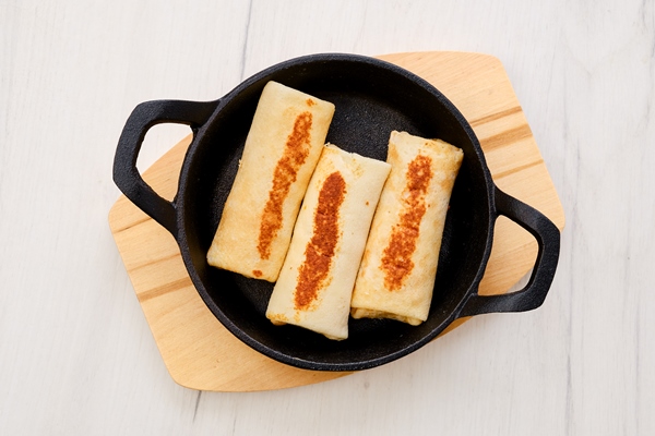 Блинчики с рыбой и маринованными огурцами top view of thin pancakes stuffed with turkey meat in cast iron skillet - Блинчики с рыбой и маринованными огурцами