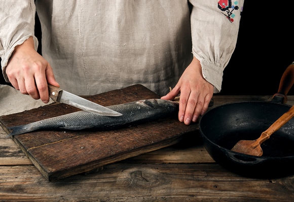 woman in gray linen clothes cleans the fish sea bass scales - Учим детей готовить отварную рыбу