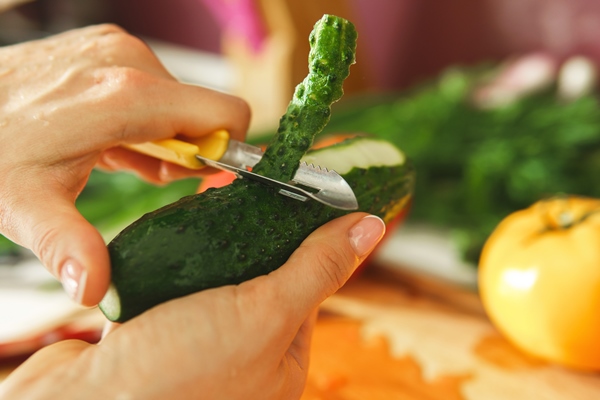 closeup of female hand with peeler and cucumber - Постный майонез с огурцами