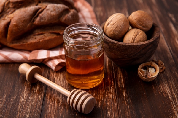 front view honey in a jar with walnuts and a loaf of black bread on a wooden background - Тыква с яблоками и мёдом