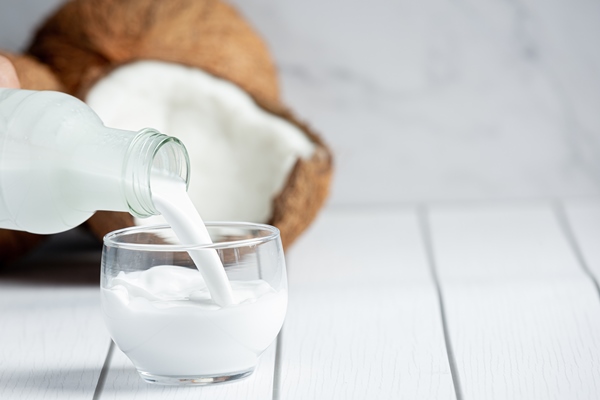 hand pouring coconut milk from bottle to glass - Бананы в карамели