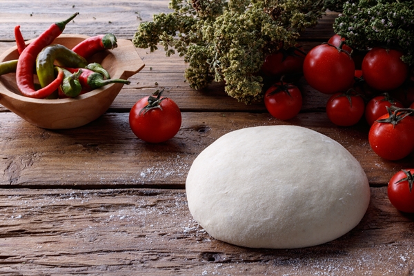lump of dough on a wooden table surrounded with tomatoes and pepper - Постная пицца с грибами и овощами