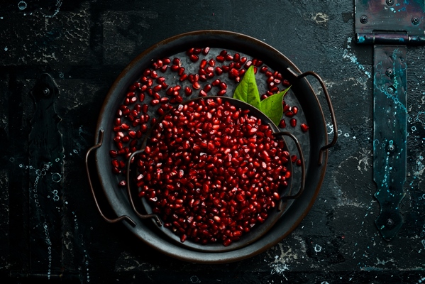 ripe pomegranate seeds on a plate fresh pomegranate fruit on a black stone background top view - Салат овощной с кунжутом и гранатом