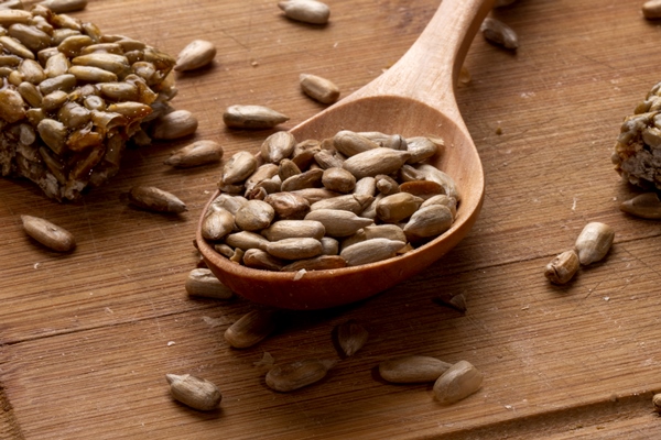 side view of a wooden spoon full of sunflower seeds with sweet kozinaki on wooden - Основы сухоядения