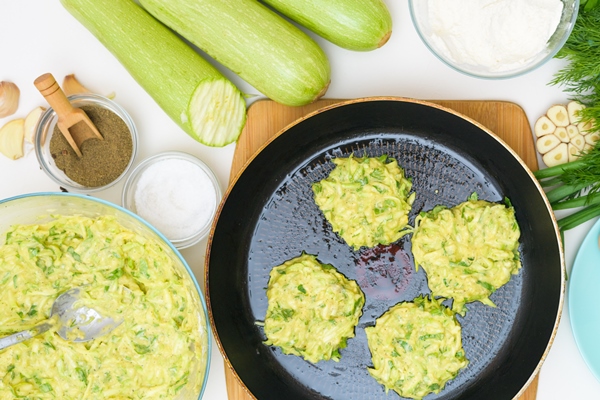 step by step recipe to cook pancakes of zucchini and greens on a light background with the addition of eggs flour garlic pepper the view from the top - Постные оладьи из кабачков