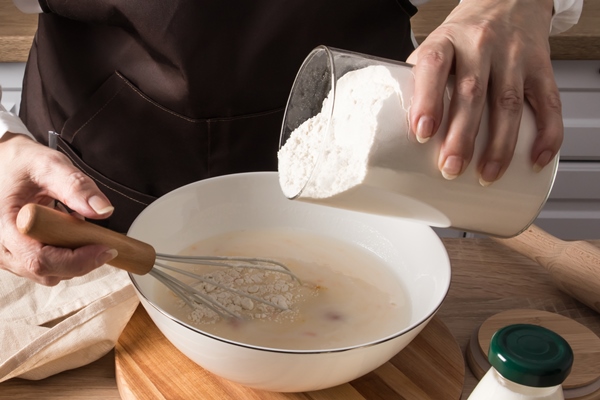 the hands of a woman in an apron pour flour from a jar into a bowl of milk the concept of cooking dough at home in the kitchen - Оладьи из печёных яблок