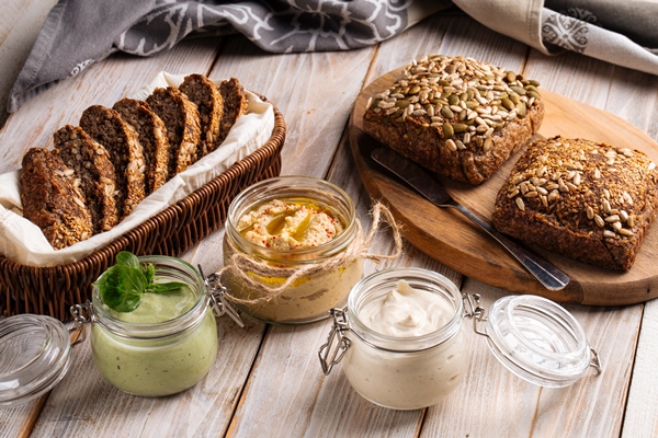 three different spreading sauces in glass jars with cut whole wheat bread on wooden boards - Бутерброды с паштетом из белой фасоли