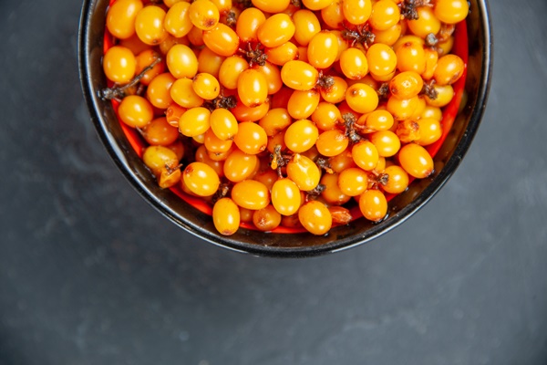 top half view sea buckthorn in bowl on dark red surface - Облепиховый чай с пряностями и лаймом