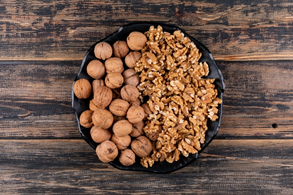 top view shelled and raw walnuts in black plate on wooden horizontal - Сациви из баклажанов по-грузински