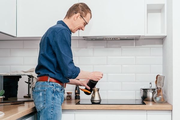 middleaged smiling man with ginger hair putting spoon of coffee from round tin in copper cezve on cooker for brewing - Американо