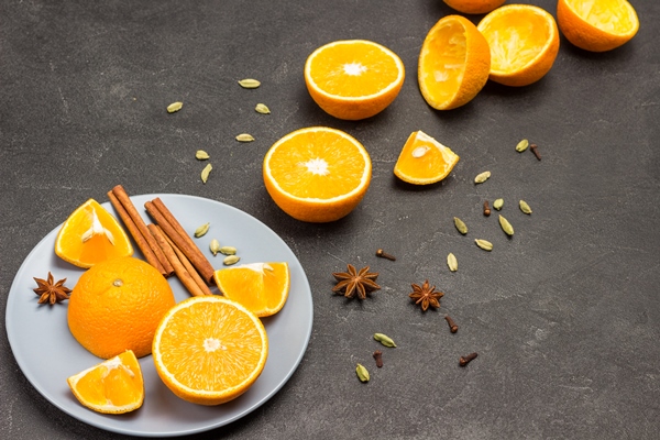 orange halves cinnamon sticks and star anise on gray plate spices on table oranges and peel on table black background copy space top view - Безалкогольный апельсиновый глинтвейн с имбирём