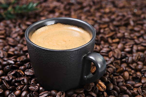 realistic view of black espresso coffee in the dark cup in the roasted coffee beans cup with coffee crema and coffee beans close up and selective focus on the cup - Кофе с пенкой без молока