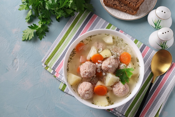 soup with chicken meatballs rice and vegetables in a white bowl on a blue background view from above - Бульон с куриными клёцками