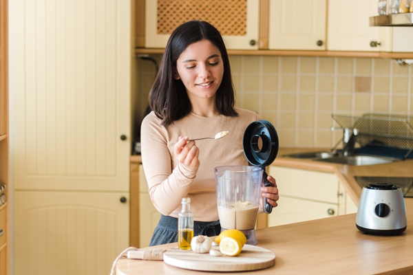 attractive woman with beautiful smile in the kitchen preparing natural vegetarian food homemade chickpeas hummus recipe - Хумус с печёным перцем