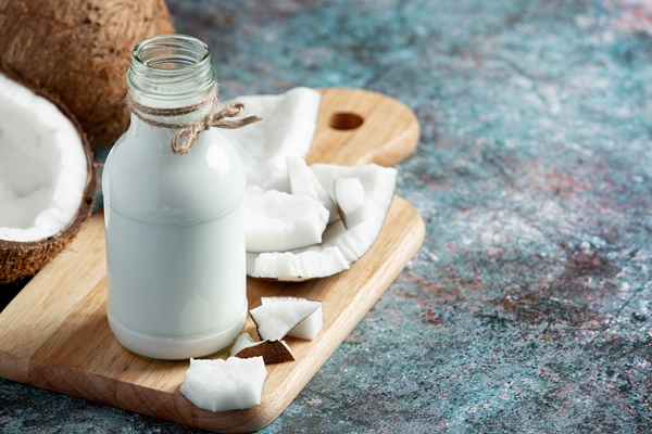 bottle of coconut milk put on wooden cutting board - Овсянка с малиной и кешью без варки