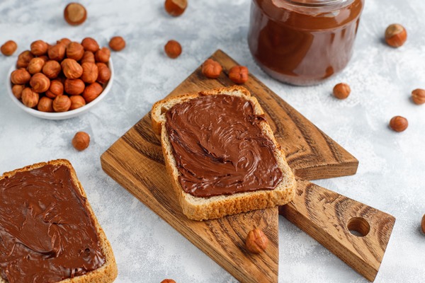 chocolate spread or nougat cream with hazelnuts in glass jar on concrete copyspace - Урбеч с какао и финиками