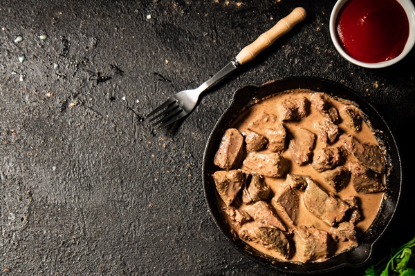 delicious fried liver in a frying pan with tomato sauce and parsley - Печень в сметане