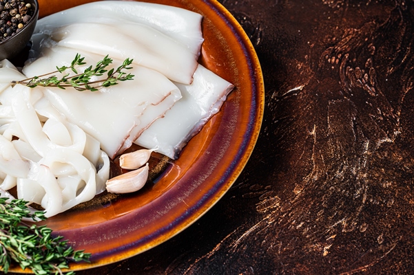 sliced raw rings calamari in a rustic plate with rosemary dark background top view copy space - Монастырская кухня: рыбный суп с кальмаром, запеканка с рыбой, салат овощной с винным уксусом