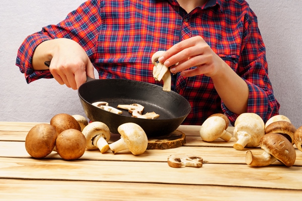 the girl puts chopped mushrooms in a pan girl in a fashionable red plaid shirt prepares food at a wooden table - Монастырская кухня: полба, сушки с маком