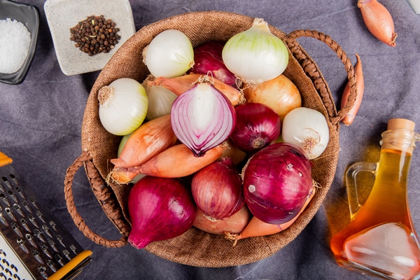 top view of different types of onion in basket with salt black pepper seeds melted butter grater around on gray cloth - Гуляш из субпродуктов