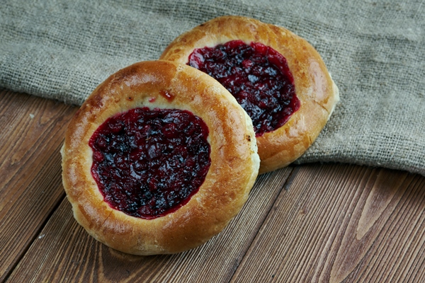 vatrushkai patties with cowberry russian pastry on a wood background - Сдобные ватрушки